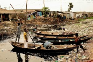 Children and wooden boats on a polluted river in Lagos, Nigeria, depicting everyday life and environmental challenges.